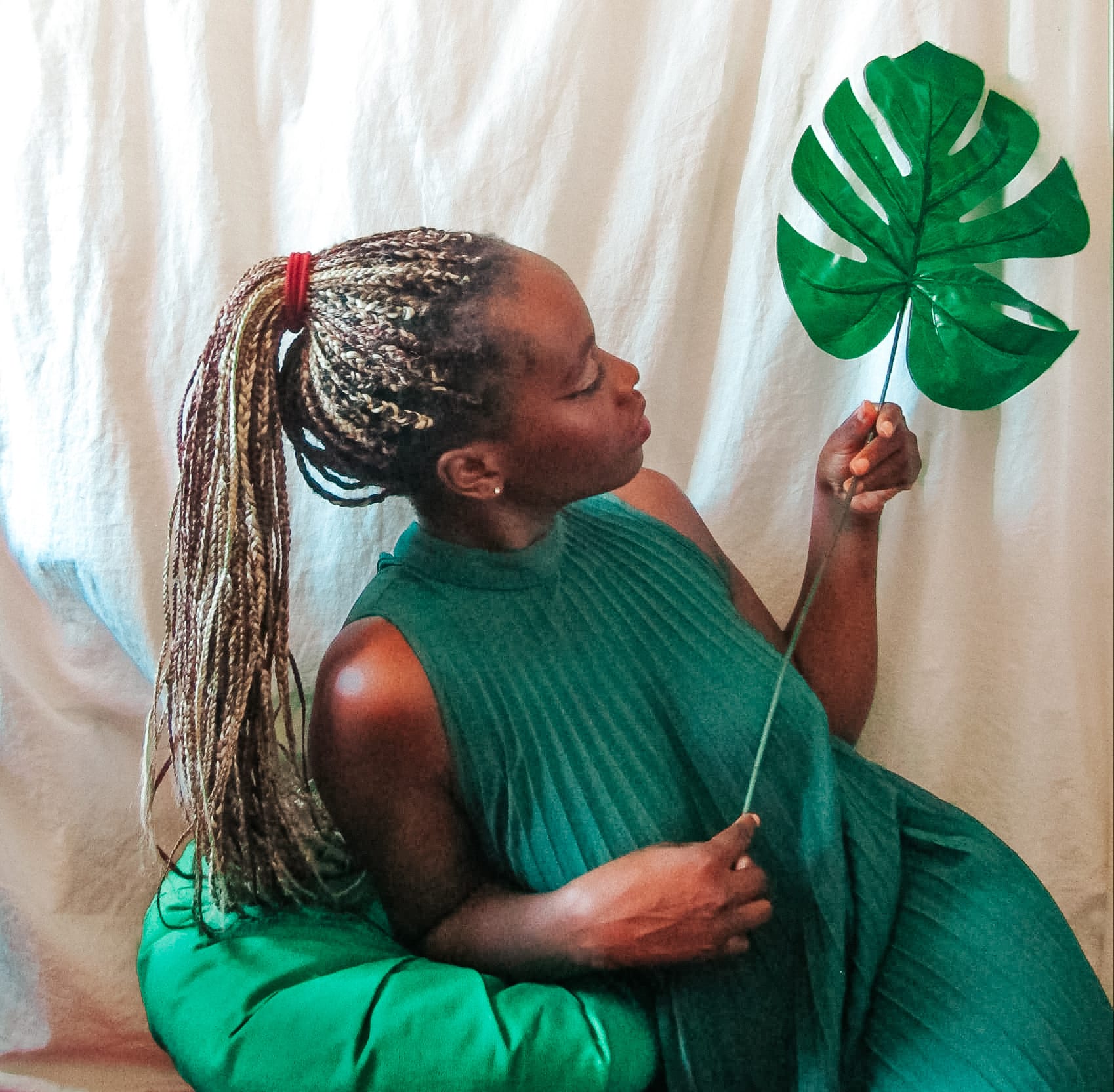 self-portrait - woman sitting on a green pillow holding a leaf in a playful manner