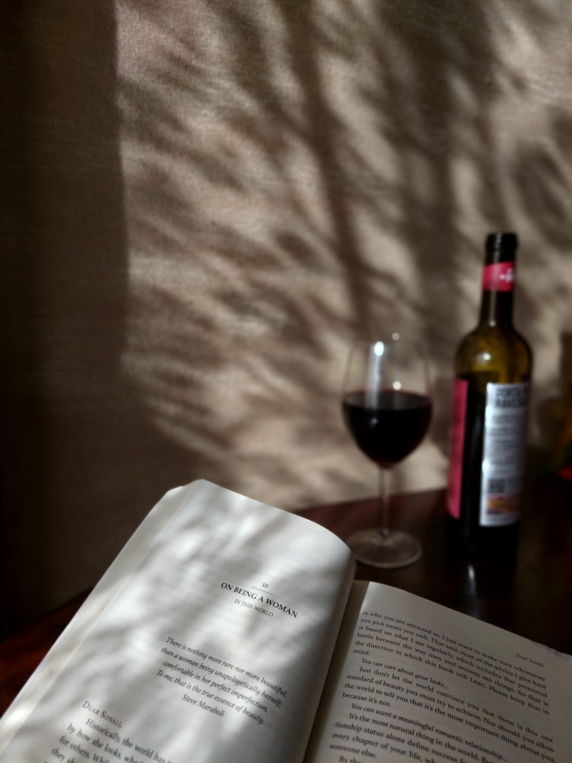 reading a book . a wine bottle and wine glass are visible in the background