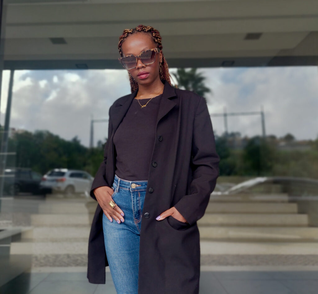 PHOTO OF A WOmAN WITH HANDS IN HER POCKETS AND WERARING SUNGLASSES, A BLAZER, BLACK SHIRT AND JEANS